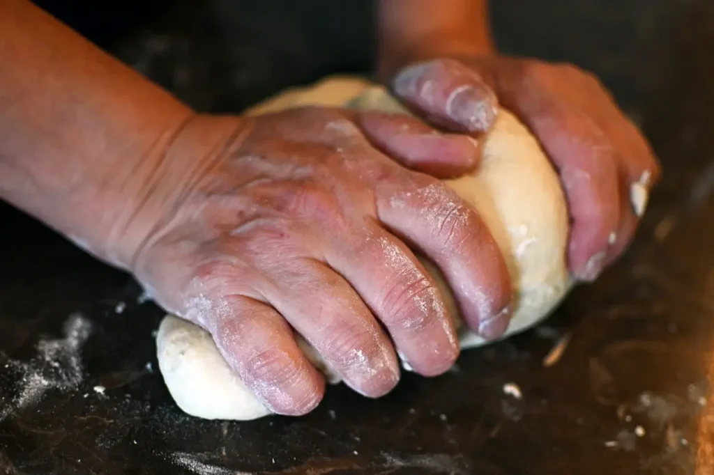 Two flour-covered hands kneading white sourdough discard bread dough on a flat surface.