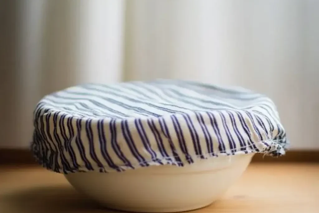 A bowl covered with a striped cloth, allowing sourdough dicrad focaccia dough to rest and rise.