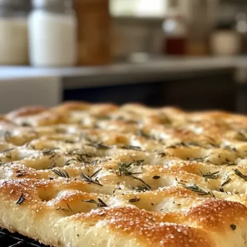 Golden-brown sourdough discard focaccia on a cooling rack, with a crispy crust, flaky sea salt, and rosemary, steaming fresh from the oven.