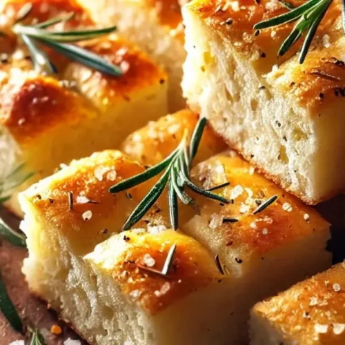 Close-up of perfectly baked sourdough focaccia squares, topped with fresh rosemary sprigs and flaky sea salt, displayed on a rustic wooden board.