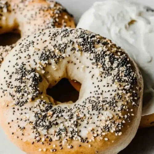 Golden brown sourdough bagels topped with sesame seeds and everything seasoning on a rustic wooden board