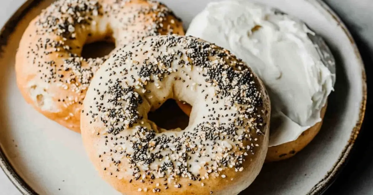 Golden brown sourdough bagels topped with sesame seeds and everything seasoning on a rustic wooden board